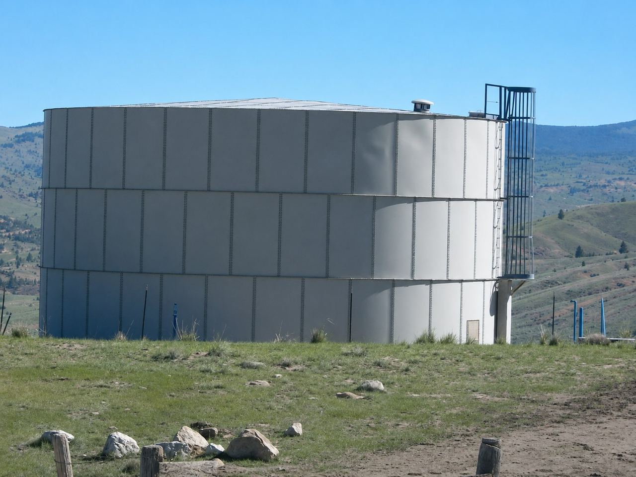 Bolted-steel ground storage tank on a hilltop with mountains behind