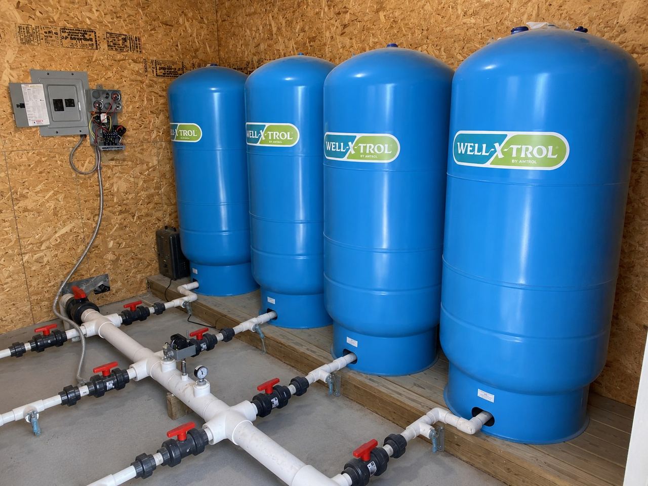 Row of blue pressure tanks and distribution manifold in a pump house