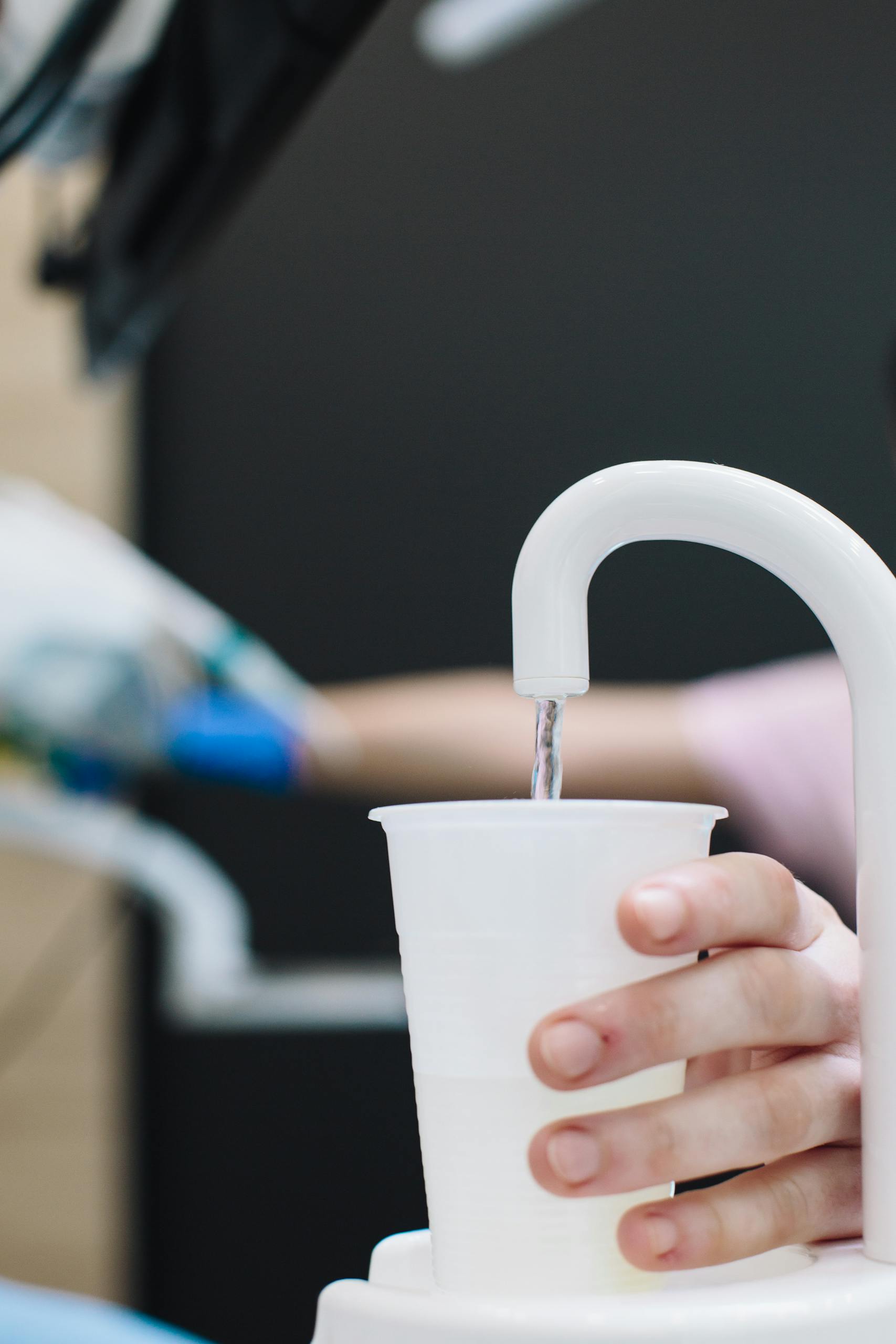 Person filling a water cup from a dispenser, representing consumer confidence in water quality