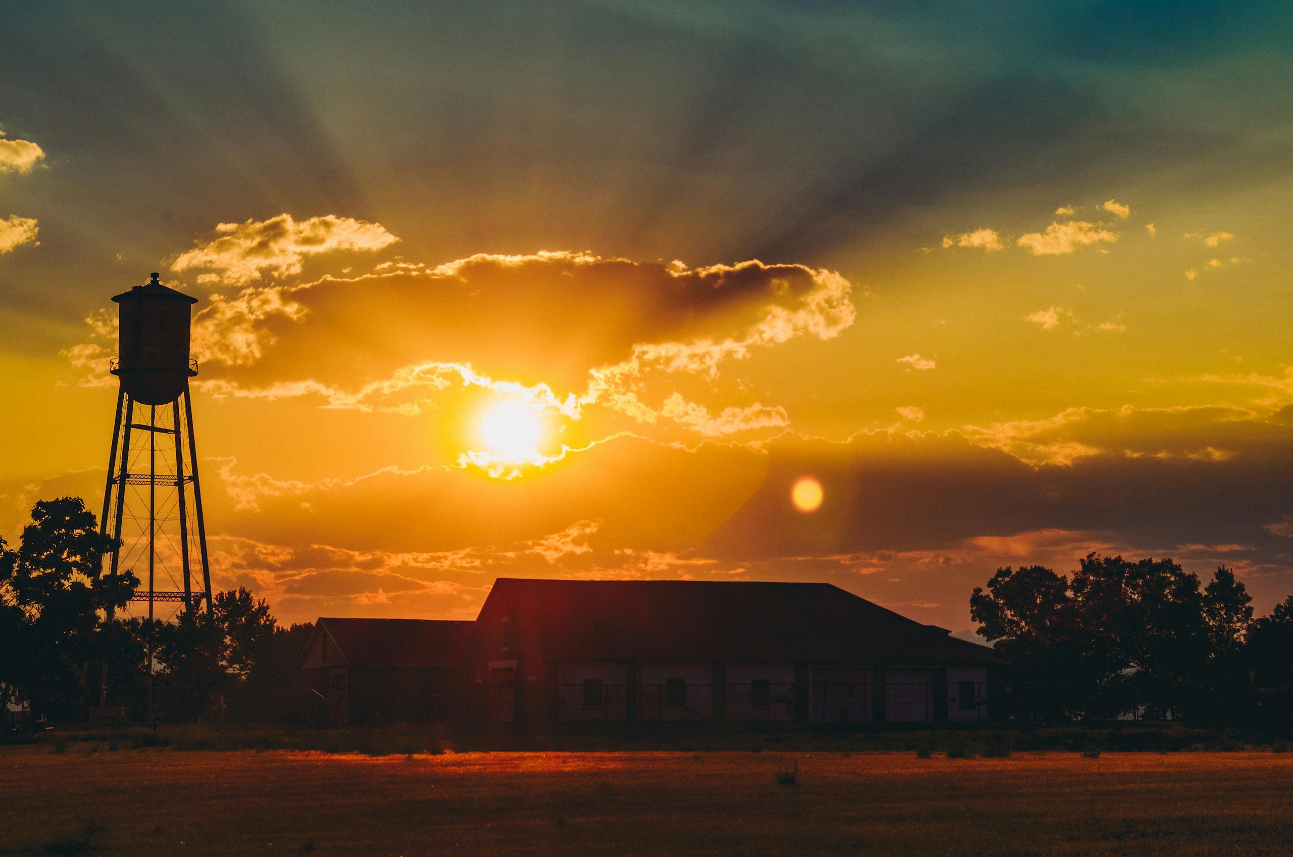 Water tower silhouetted against a dramatic sunset over a rural farm community